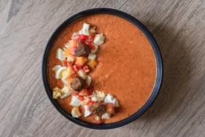 Bol de gaspacho au pain avec des croutons de pain aux drêches, de l'oeuf dur et du fromage de chèvre.